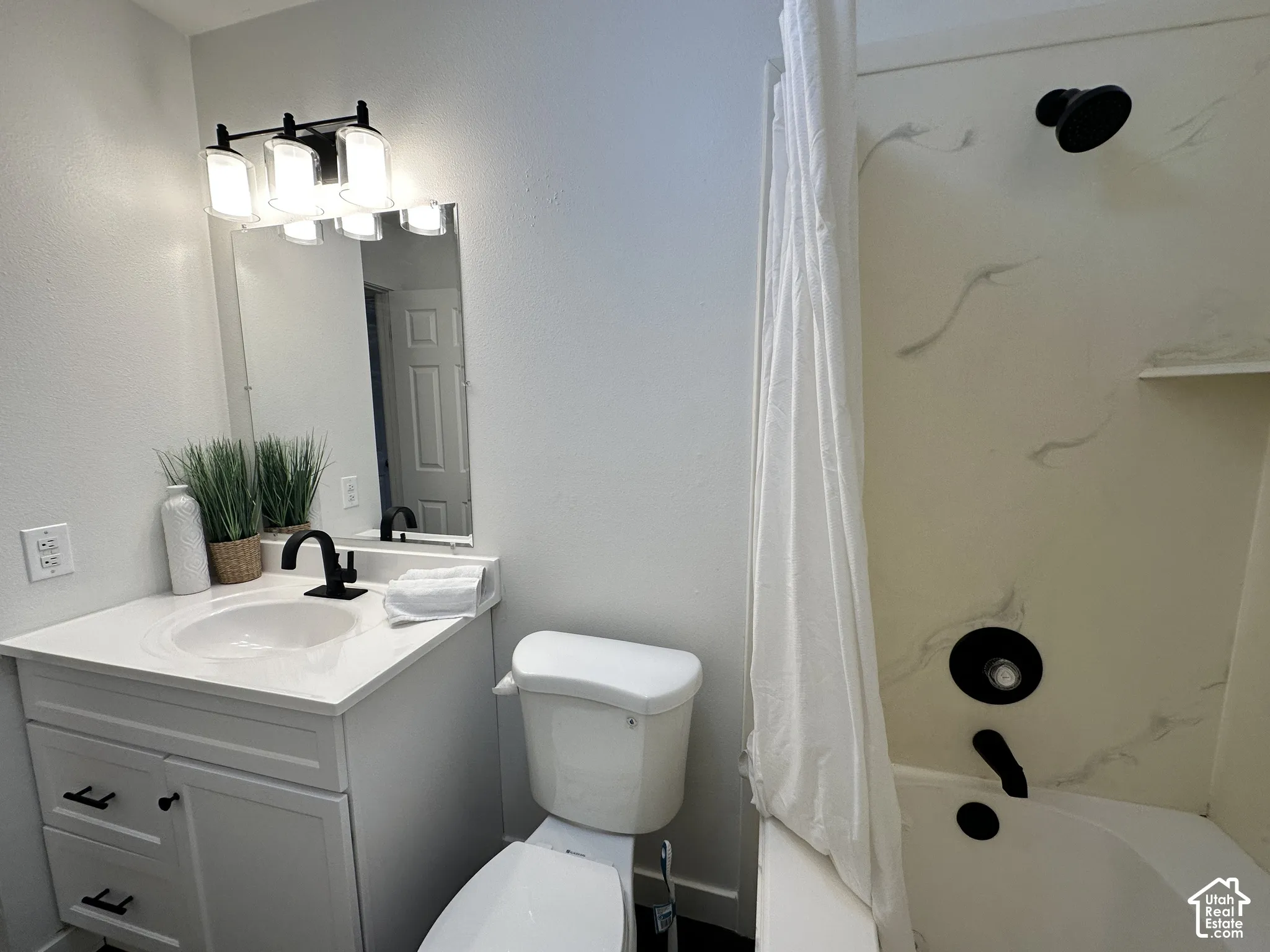 White vanity featuring a solid surface countertop, integrated sink, and matte black hardware, accompanied by a matching matte black faucet and shower fixtures, and a tub-shower combination with patterned wall surround