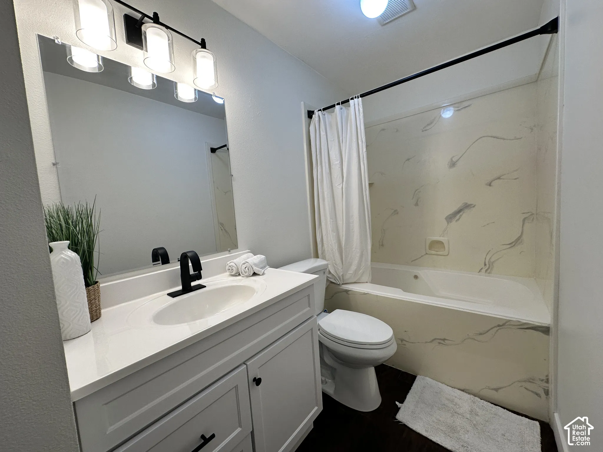 Bathroom featuring a white vanity with a solid-surface countertop, matte black faucet, wall-mounted vanity lighting, and a bathtub with a stone-patterned surround
