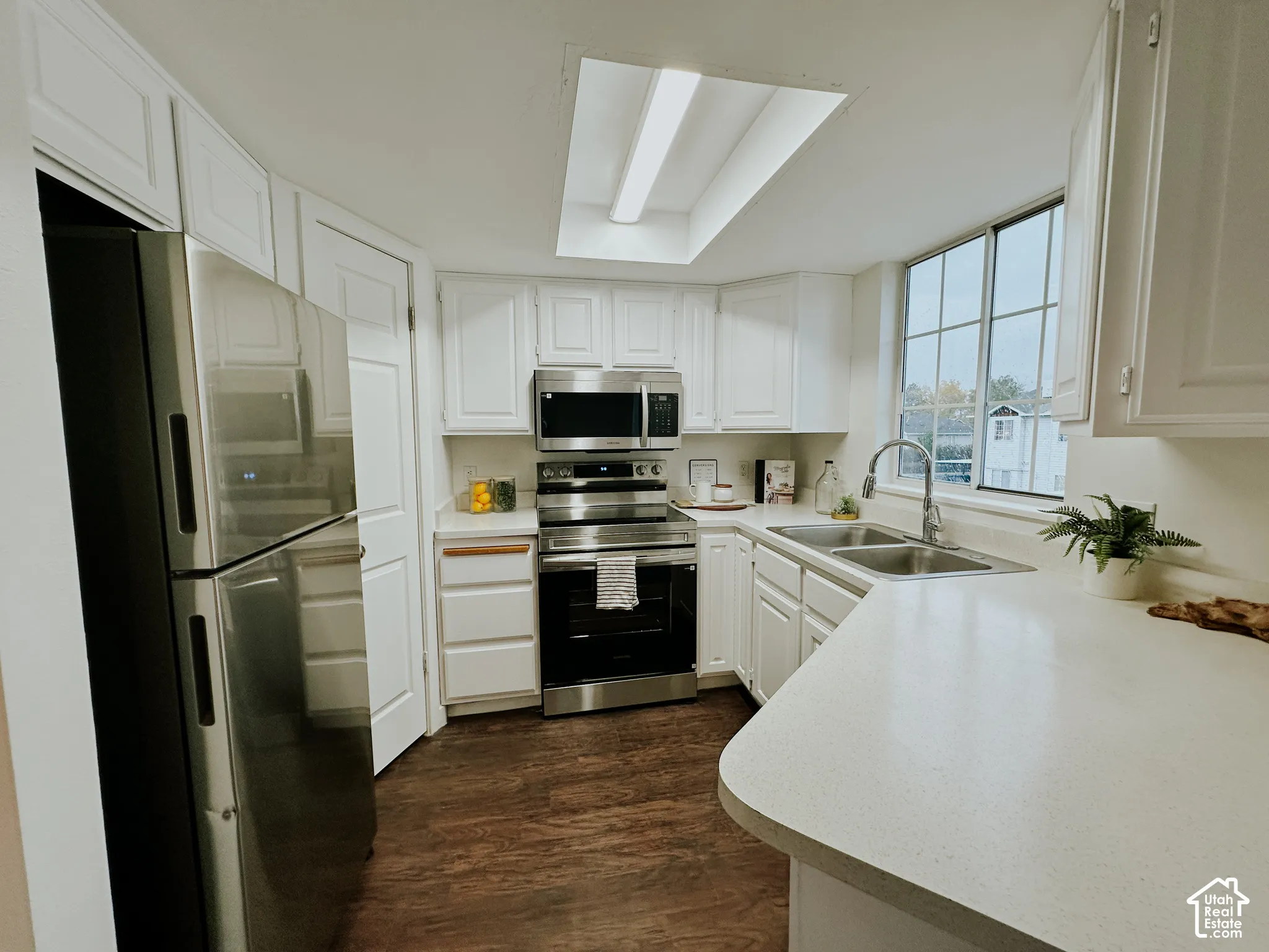 Kitchen featuring white cabinetry, stainless steel appliances, solid-surface countertops, wood-finish flooring, and a recessed skylight