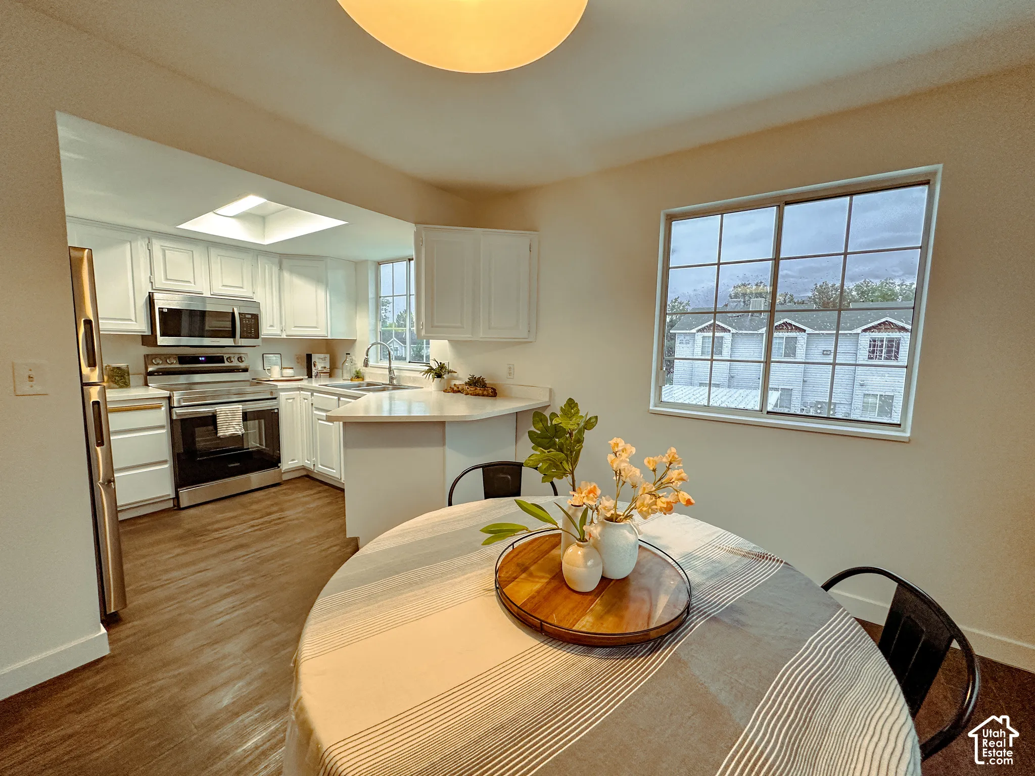 Kitchen featuring white cabinetry, stainless steel appliances, wood-finish flooring, a skylight, and a grid-pattern window