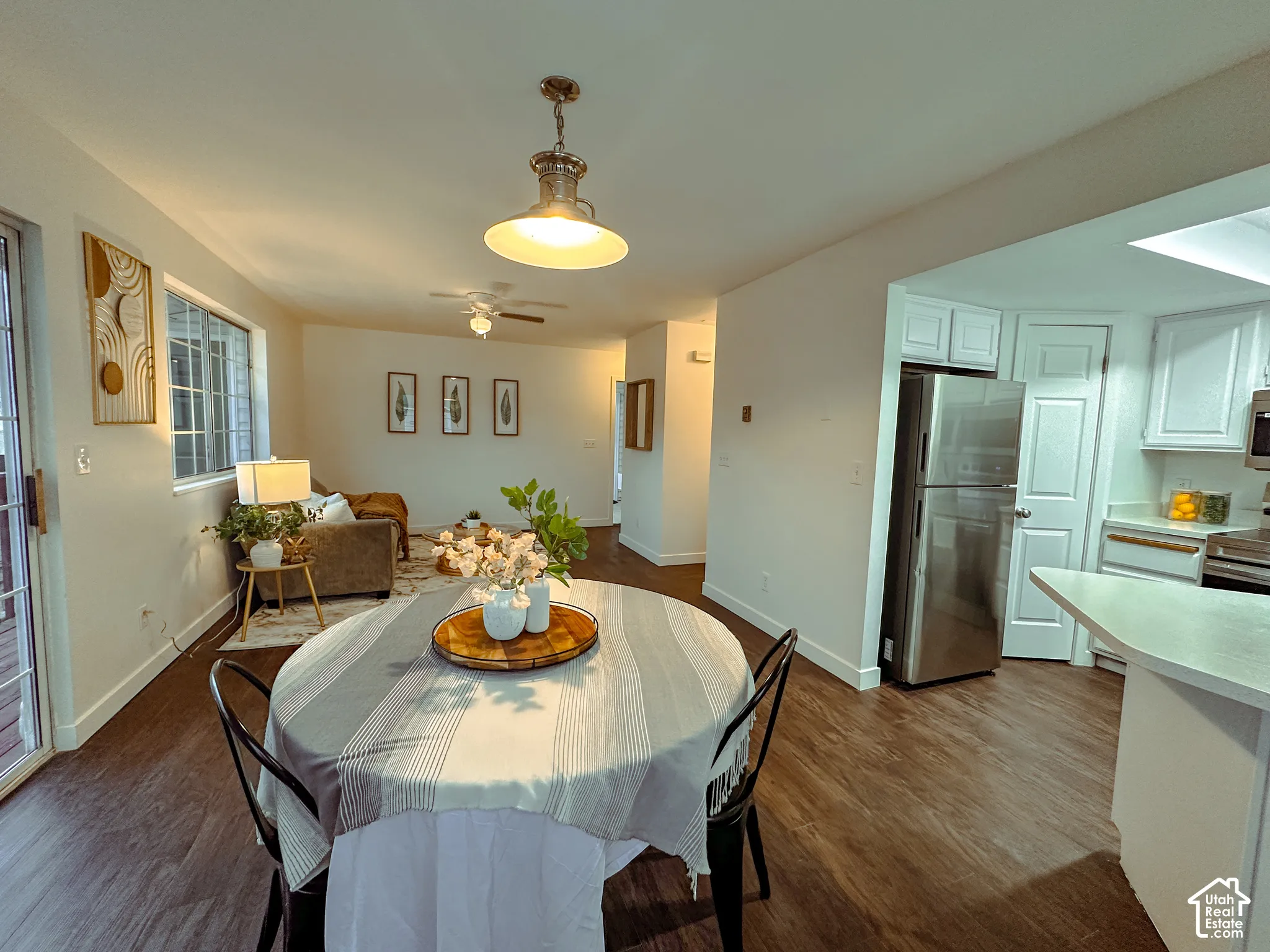 Open-concept interior featuring wood-finish flooring, a stainless steel refrigerator, white cabinetry, and a tiered pendant light fixture