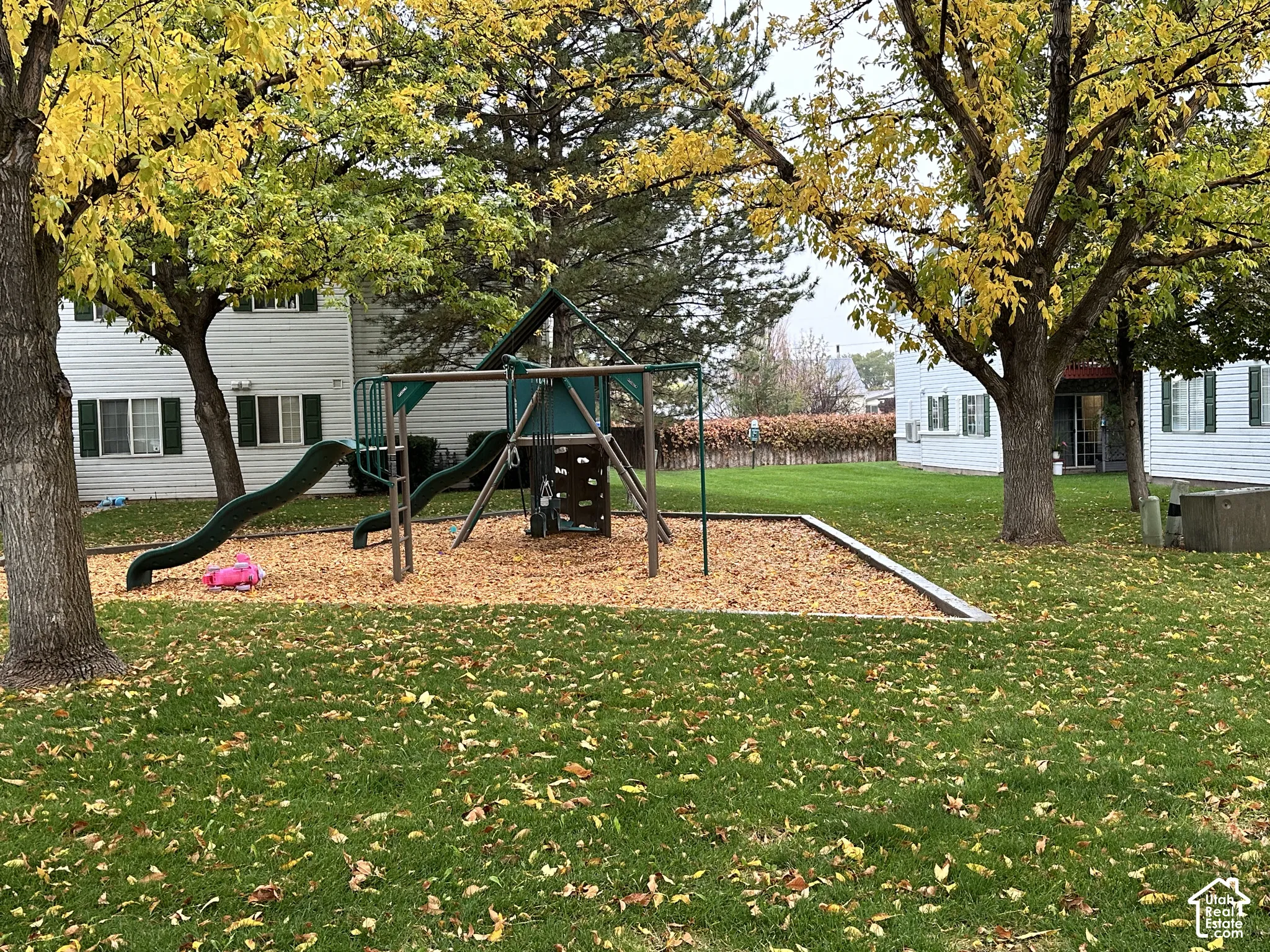 Common grounds featuring a playground structure with a slide and climbing wall, surrounded by mature trees and a manicured lawn