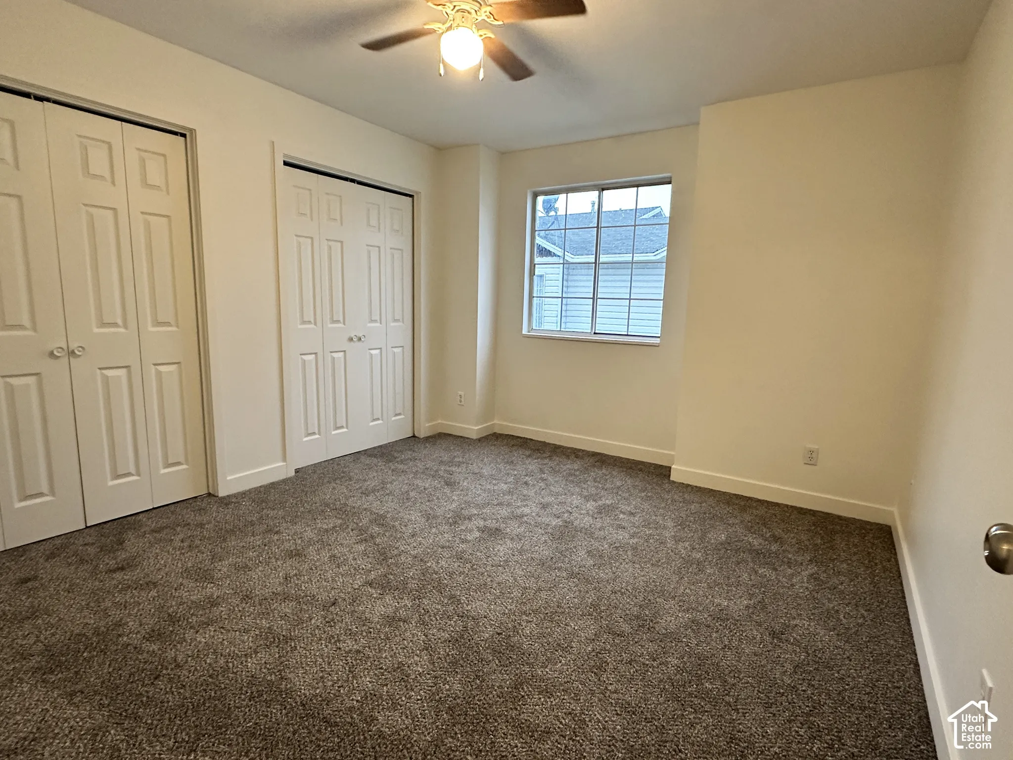 Room featuring neutral wall tones, wall-to-wall carpeting, two sets of double-panel closet doors, and a ceiling-mounted light fixture with fan