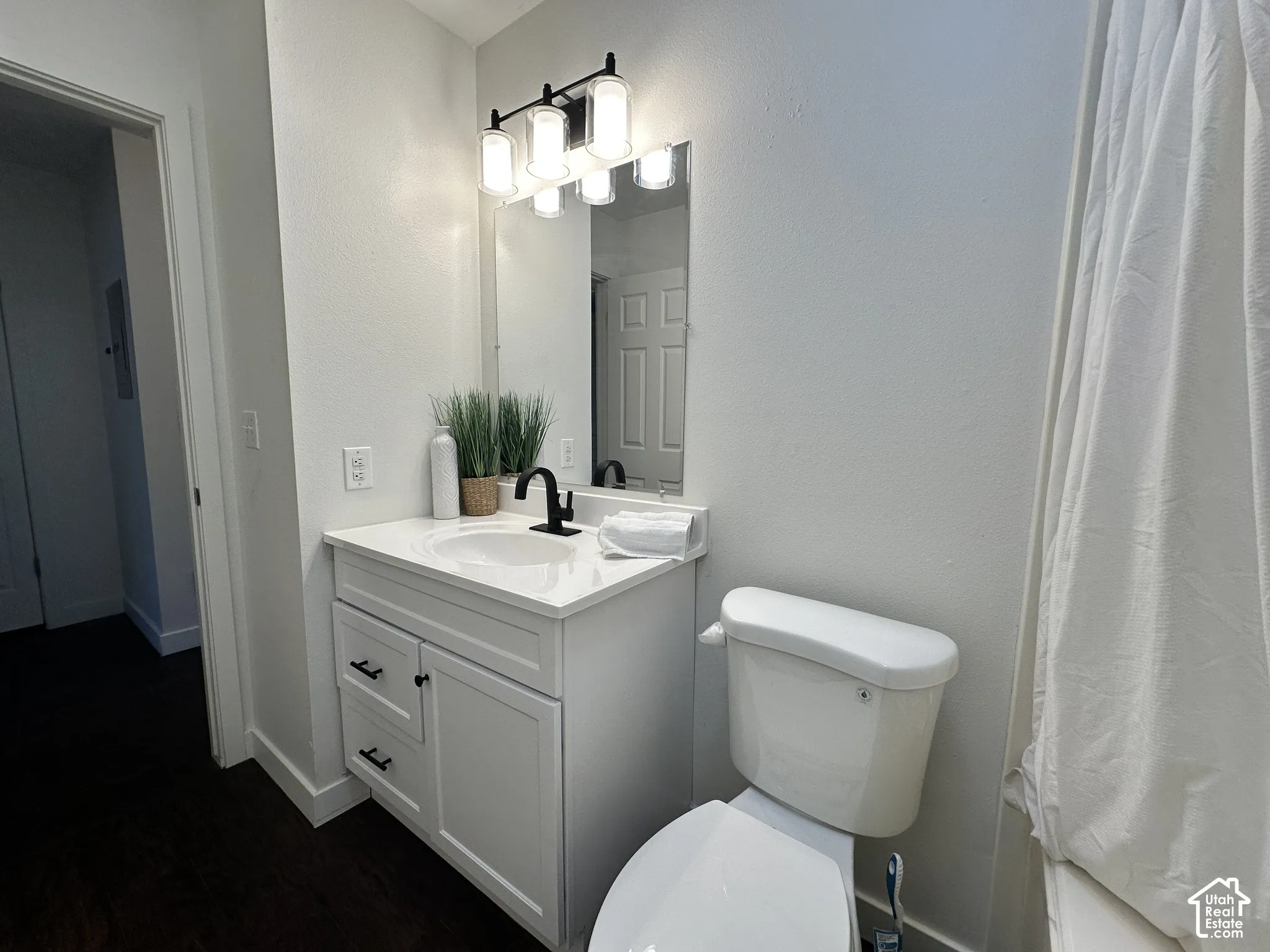 Bathroom featuring a white vanity cabinet with shaker-style doors, a solid-surface countertop with an integrated basin, a matte black high-arc faucet, and a contemporary four-light vanity fixture