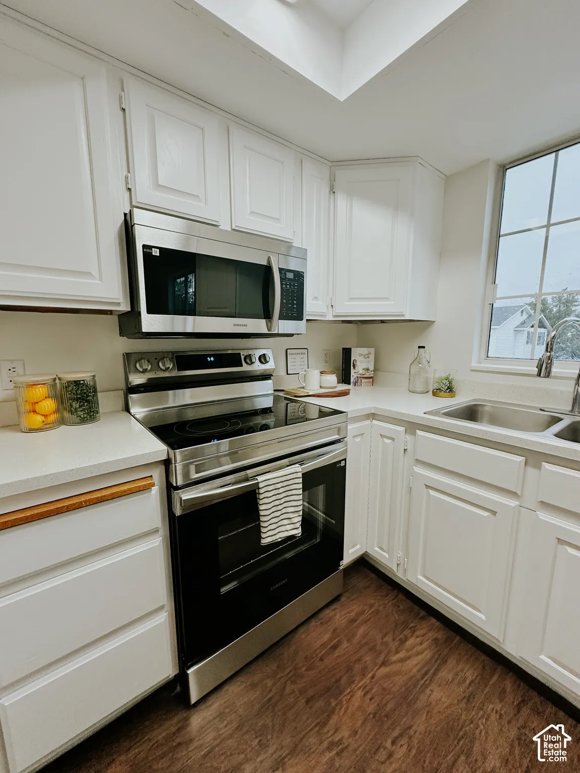 Kitchen featuring white shaker-style cabinetry, solid-surface countertops, stainless steel appliances, a skylight, and wood-finish flooring