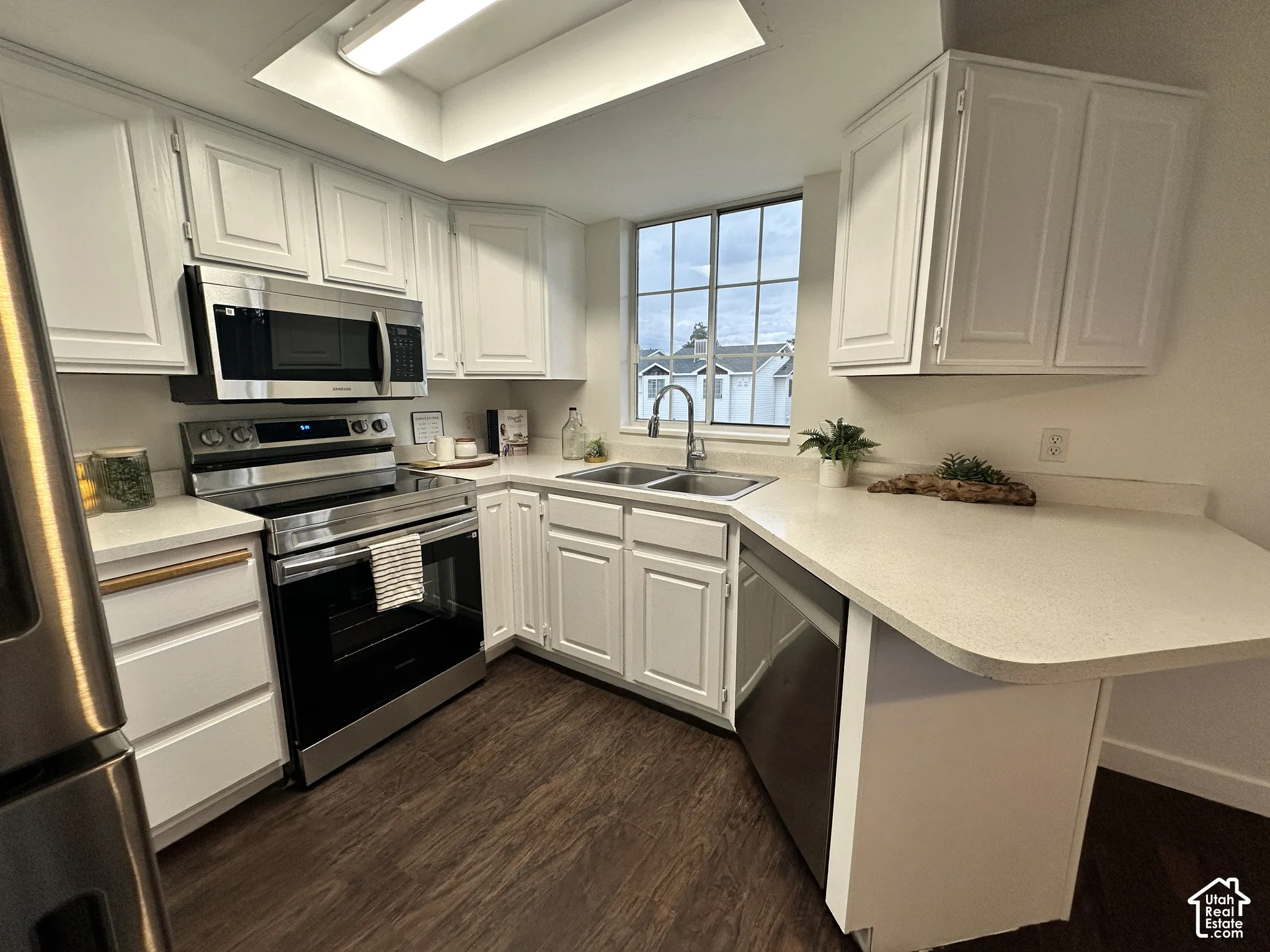 Kitchen featuring white cabinetry, stainless steel appliances, solid surface countertops, a dual-basin undermount sink, and wood-finish flooring