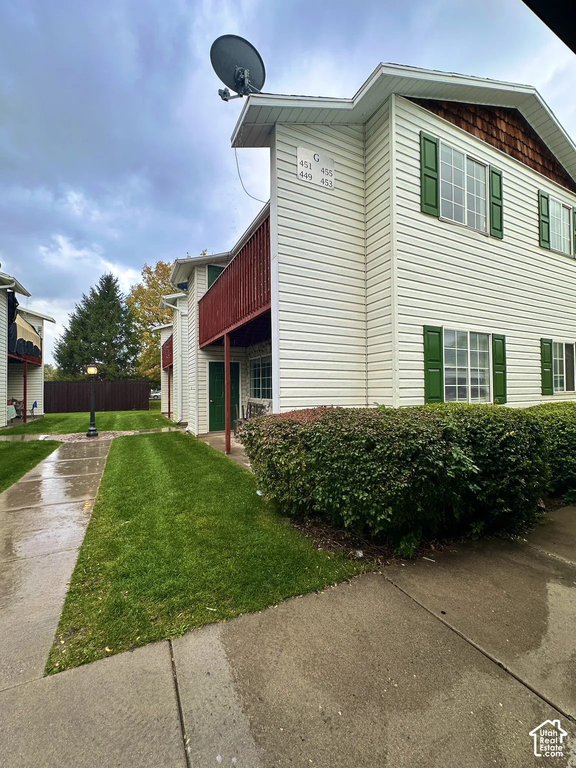 Multi-story exterior featuring light-colored horizontal siding, dark decorative window shutters, wood-tone shingle accents, and a covered balcony
