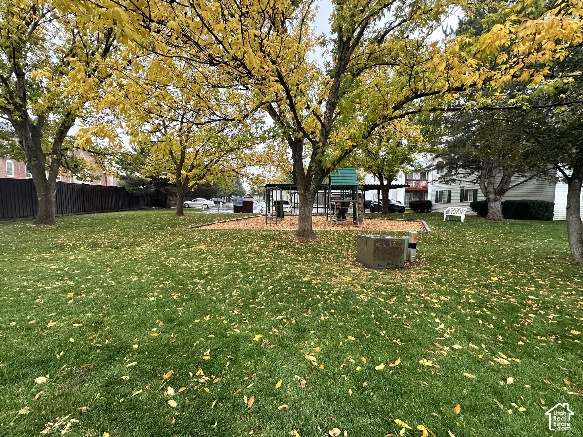 Expansive grass lawn featuring mature trees, a wood-mulched play area, and perimeter fencing