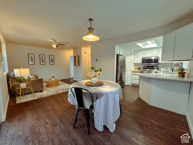Open concept interior featuring wood-finish flooring, white shaker-style cabinetry, stainless steel appliances, a breakfast bar, and a ceiling-mounted pendant light