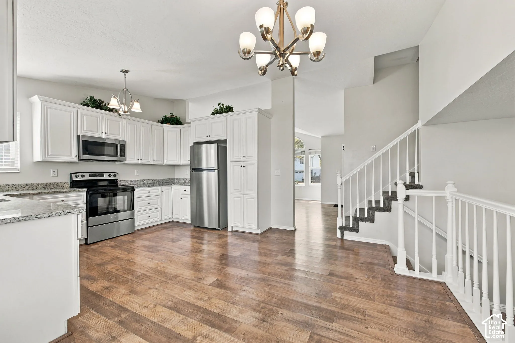 Kitchen featuring white cabinetry, stone-finish countertops, stainless steel appliances, wood-finish flooring, and a multi-arm chandelier