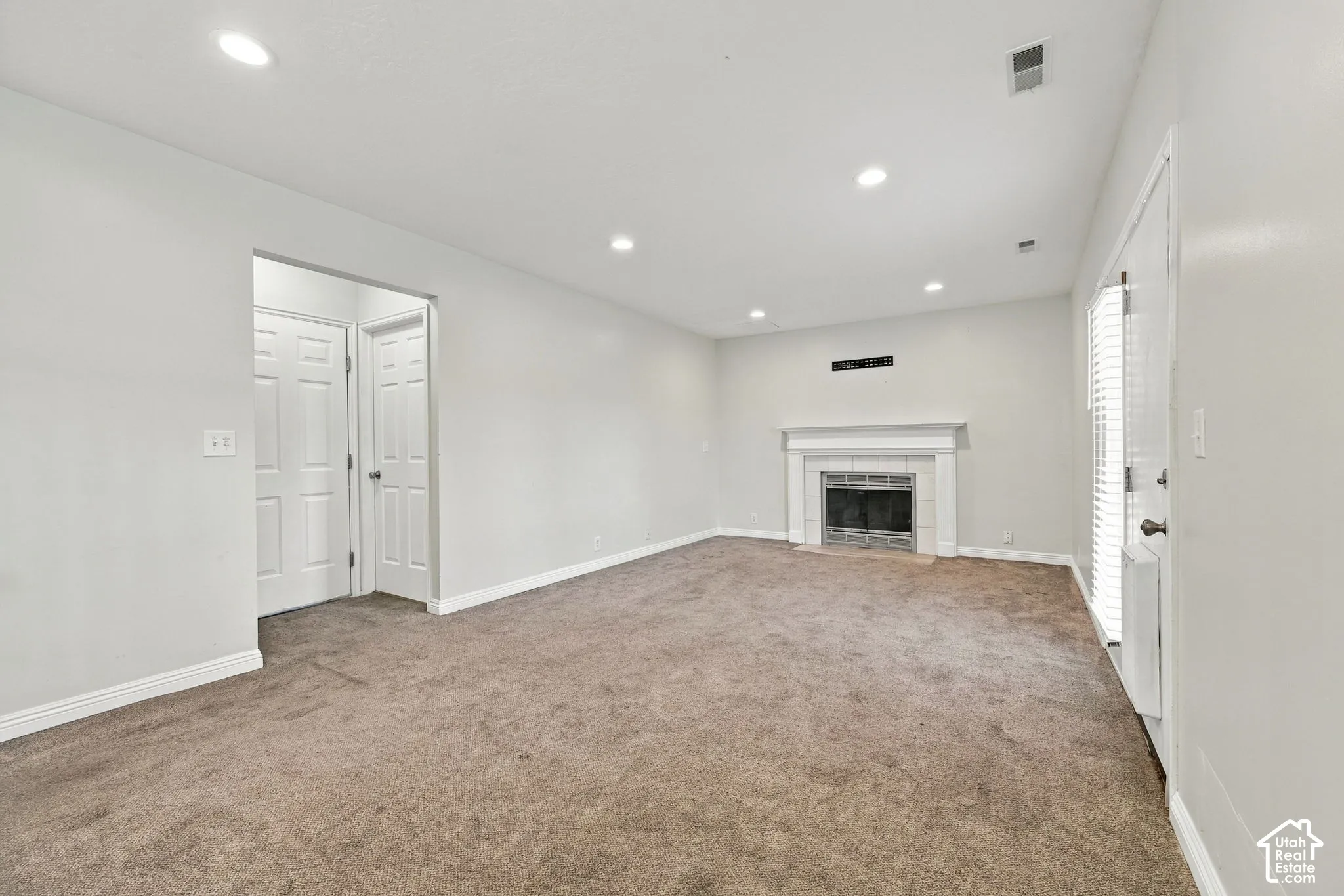 Living area featuring neutral carpeting, recessed ceiling lighting, and a white fireplace surround with a mantel