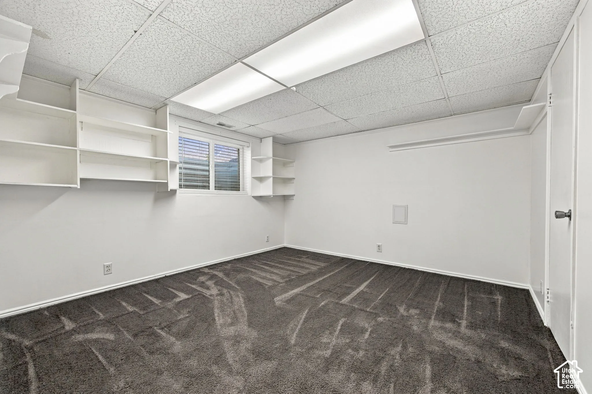 Room featuring wall-to-wall carpeting, built-in shelving, a drop ceiling with recessed lighting, and a window