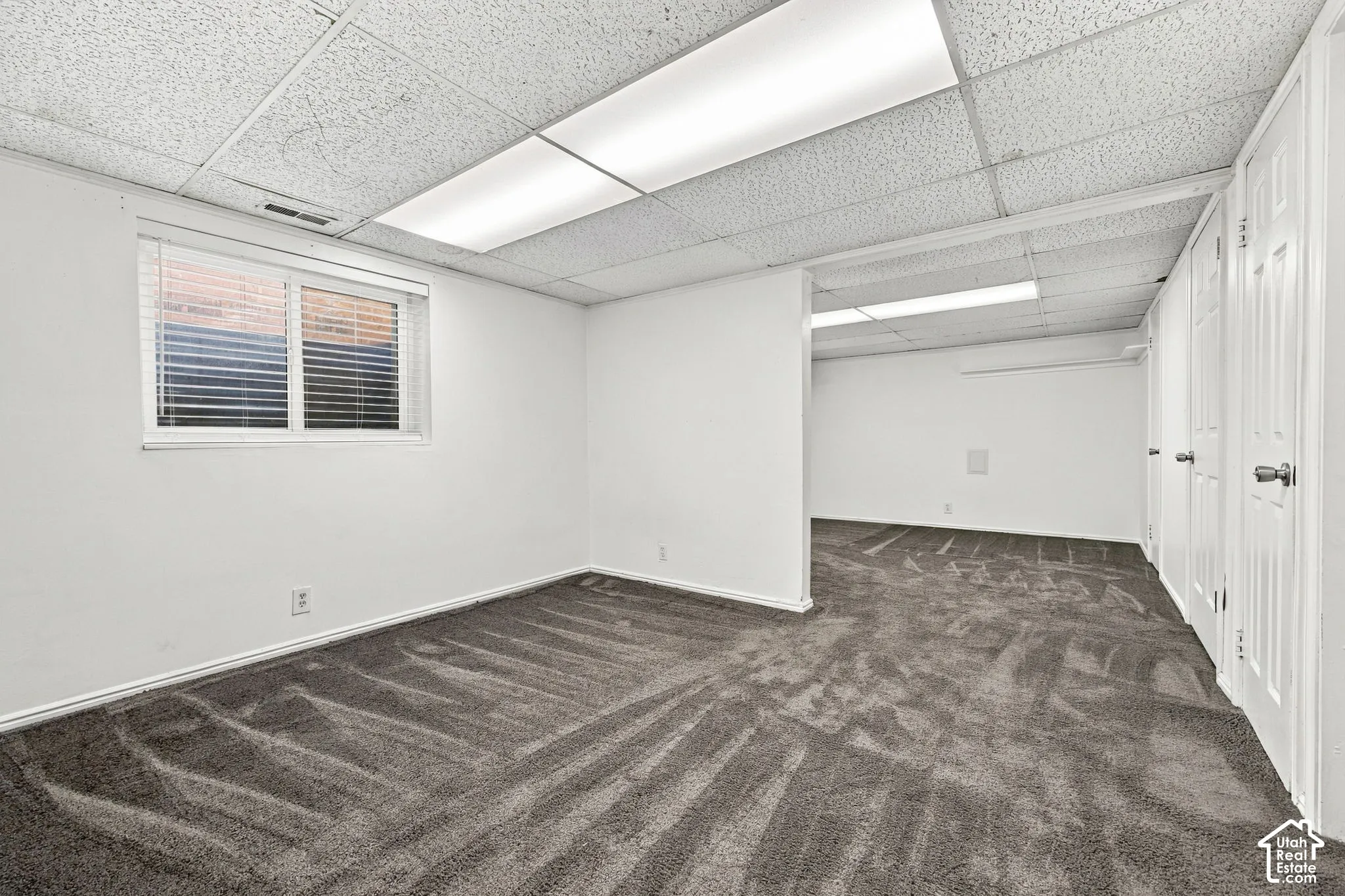 Finished room featuring wall-to-wall carpeting, drop ceiling with integrated rectangular lighting, and sliding panel doors