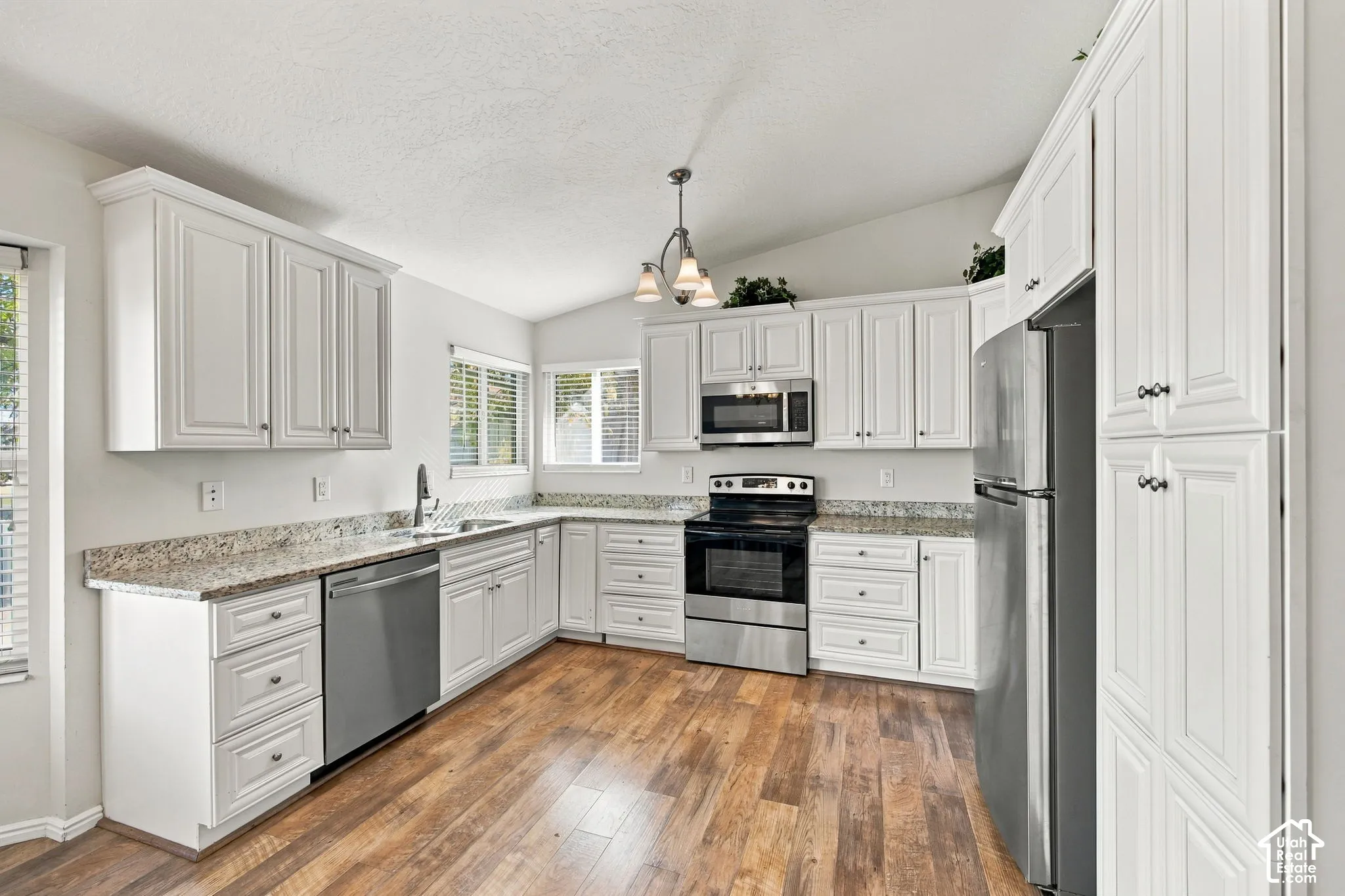 Kitchen featuring white cabinetry, stone-finish countertops, stainless steel appliances, wood-finish flooring, and a vaulted ceiling