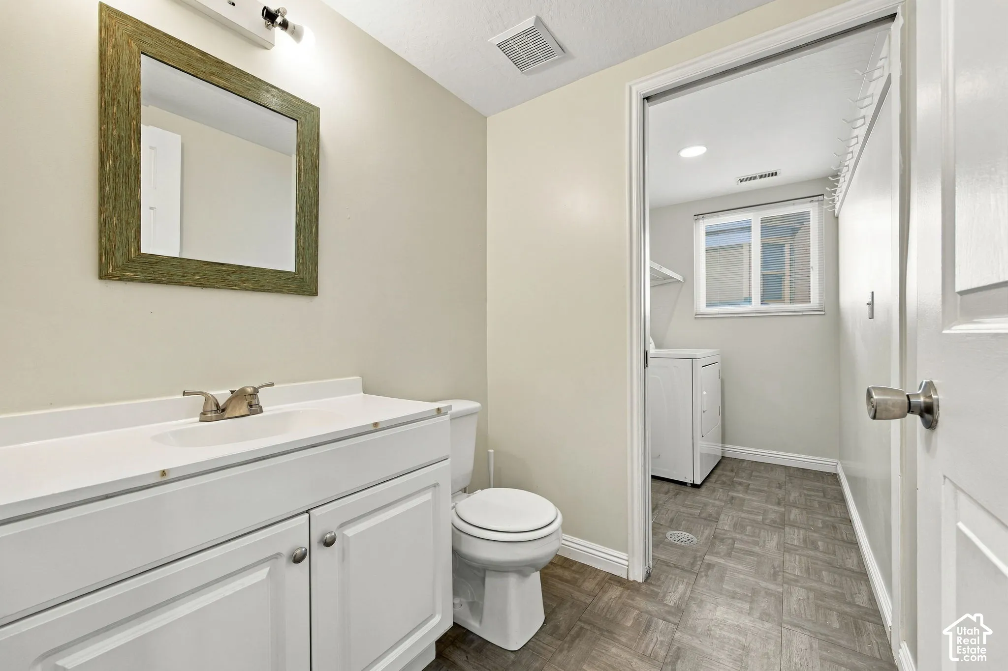 Bathroom featuring a white vanity cabinet with a solid surface countertop, undermount sink, brushed metal faucet, and framed wall mirror, with tile-patterned flooring