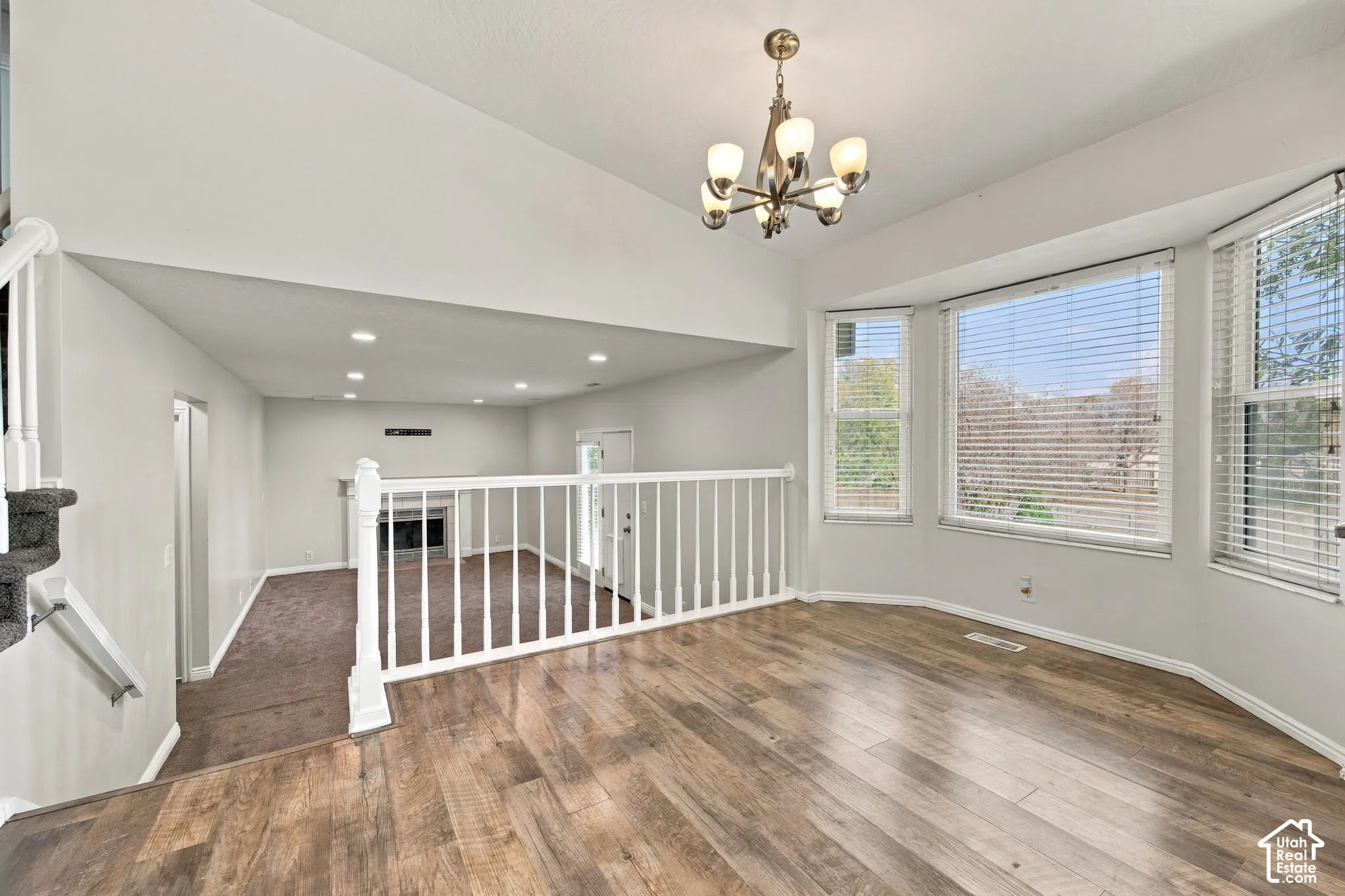 Vaulted ceilings, wood-finish flooring, bay windows with integrated blinds, multi-arm chandelier, and a fireplace with a decorative mantel