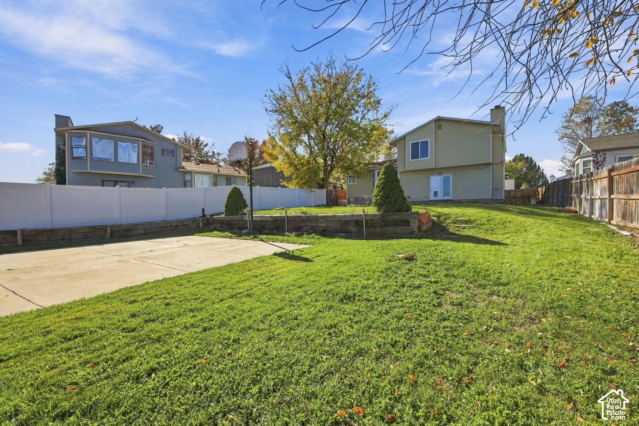 Rear exterior grounds featuring a concrete pad, tiered landscaping with timber retaining walls, and a perimeter of vinyl and wood fencing
