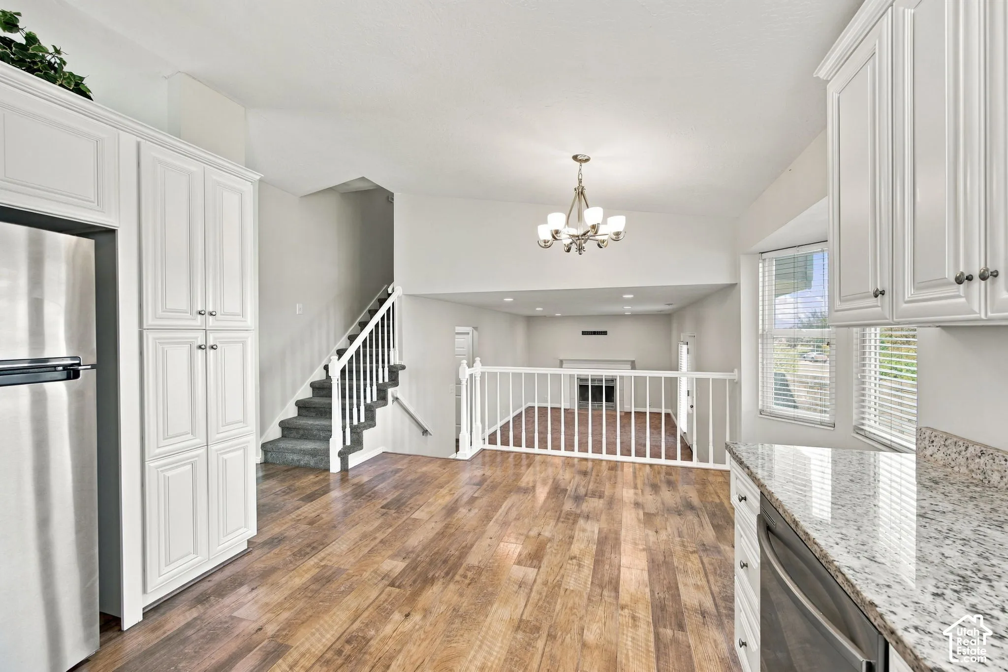 Kitchen featuring white cabinetry, stone-finish countertops, stainless steel appliances, wood-finish flooring, and a multi-arm chandelier