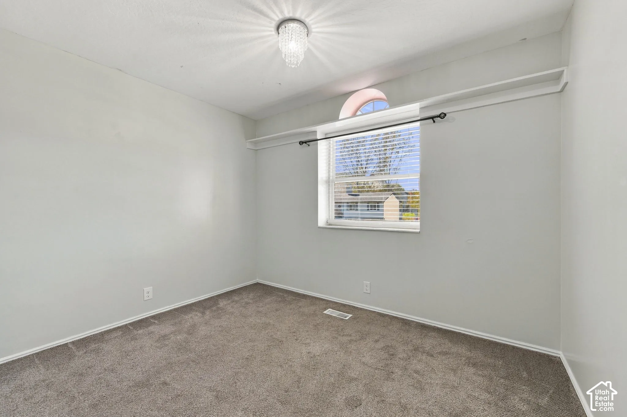 Room featuring neutral carpeting, a crystal-accented flush-mount light fixture, a window with an arched transom, and integrated shelf storage