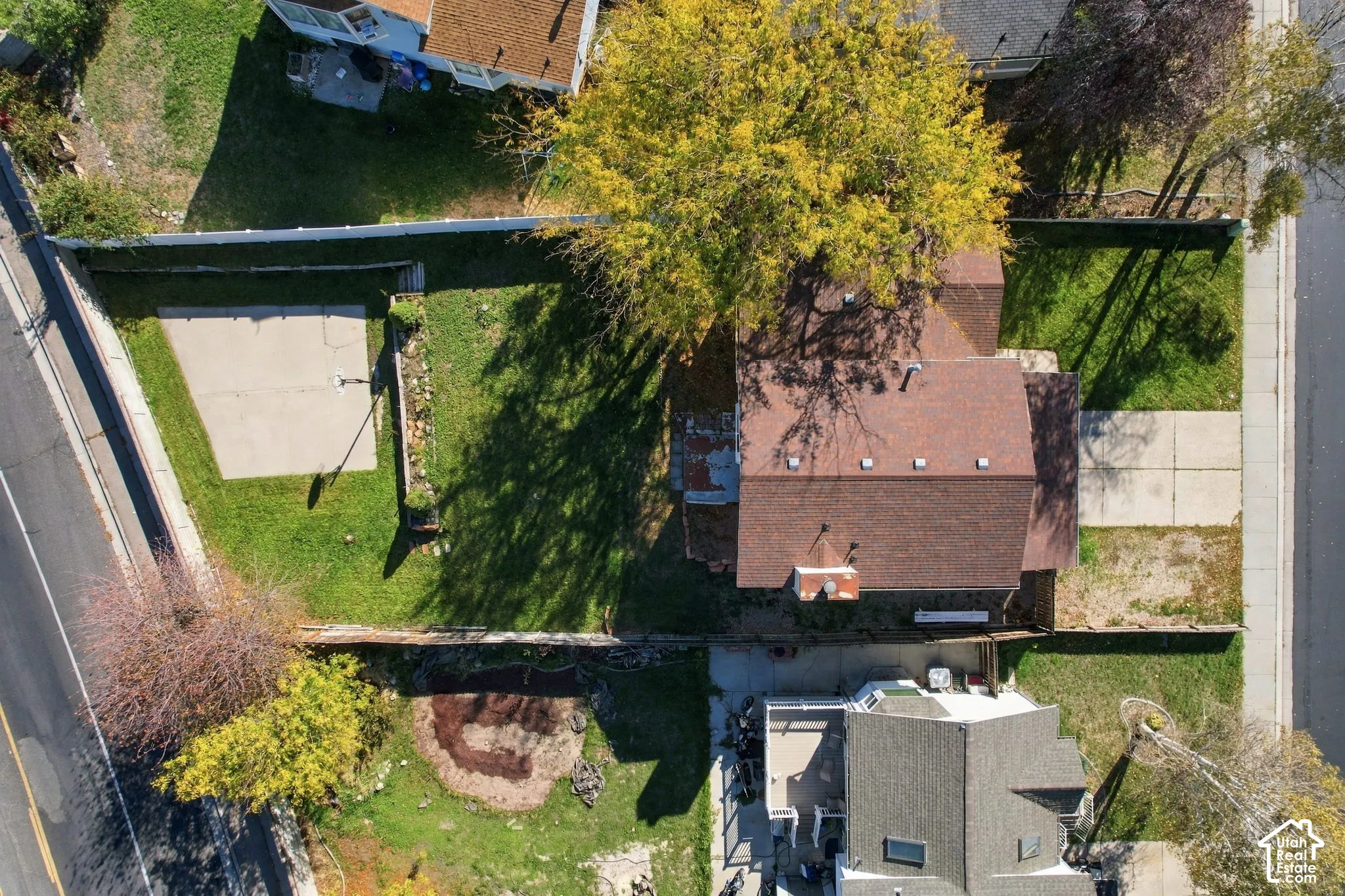 Aerial perspective of property featuring a fenced backyard, concrete parking area, mature trees, and shingle roofing