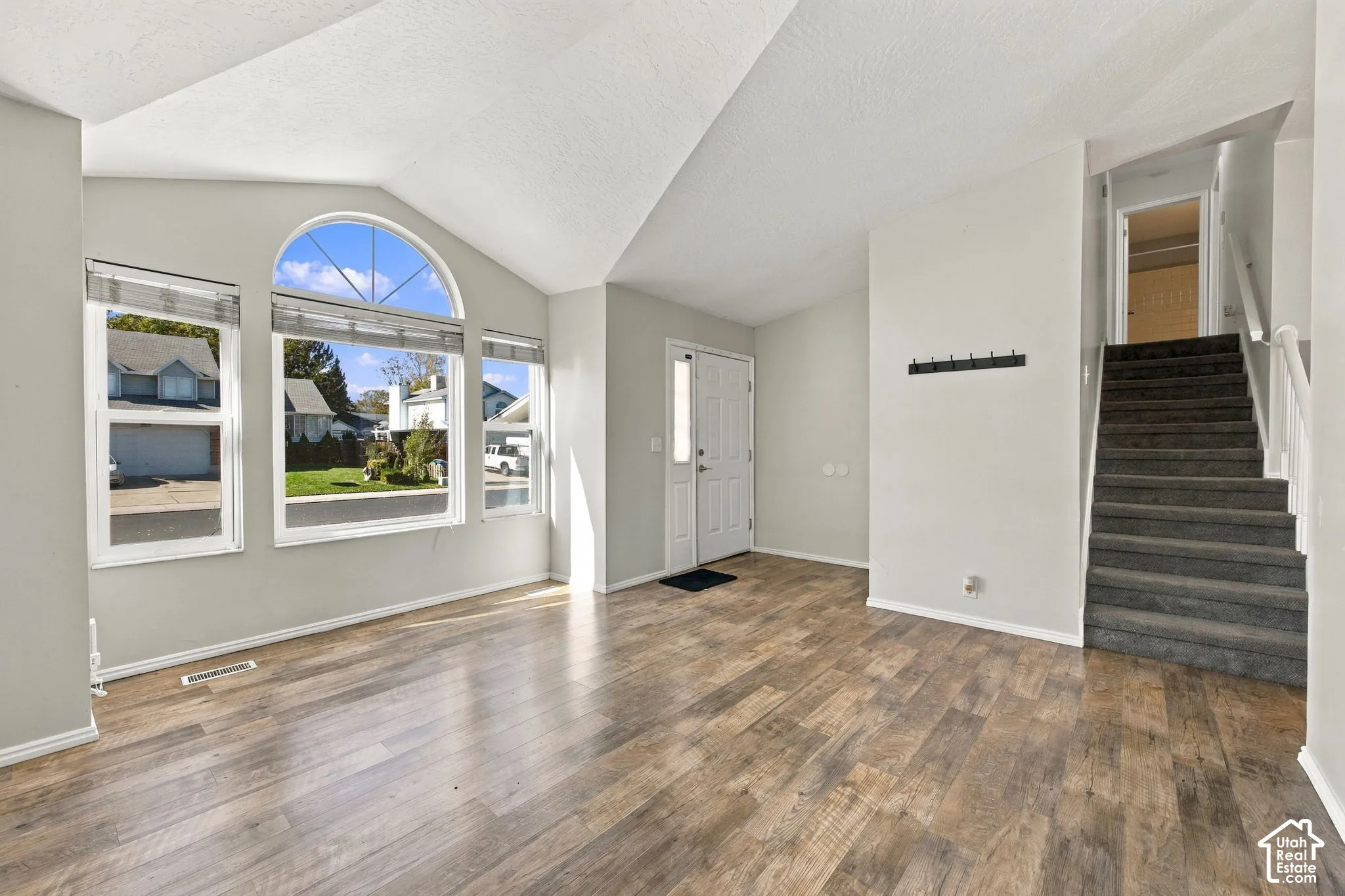 Vaulted ceiling living area featuring wood-finish flooring, an arched window, and a staircase with carpeted treads