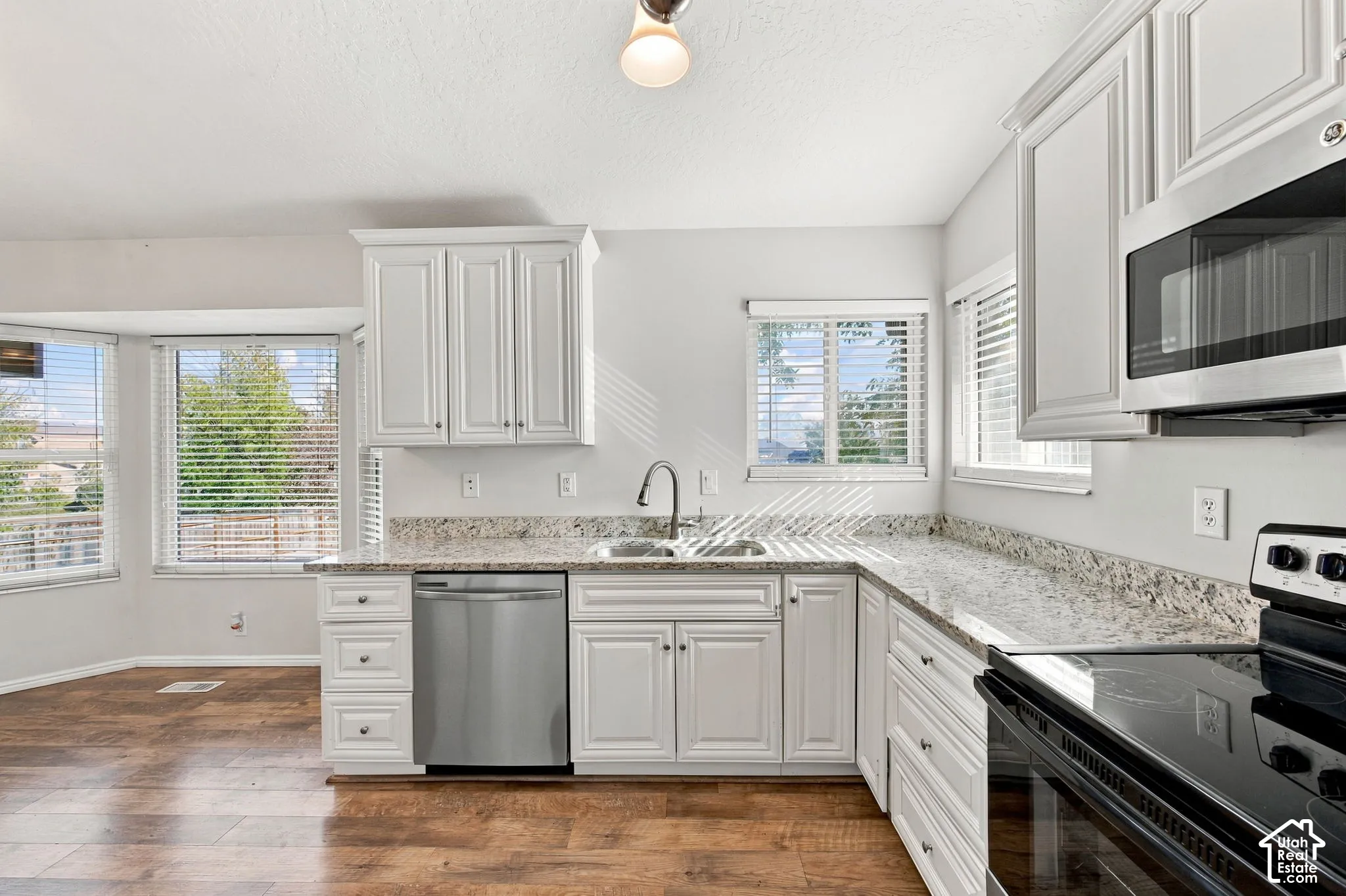 Kitchen featuring white cabinetry, stone-surface countertops, wood-finish flooring, stainless steel dishwasher, and built-in microwave