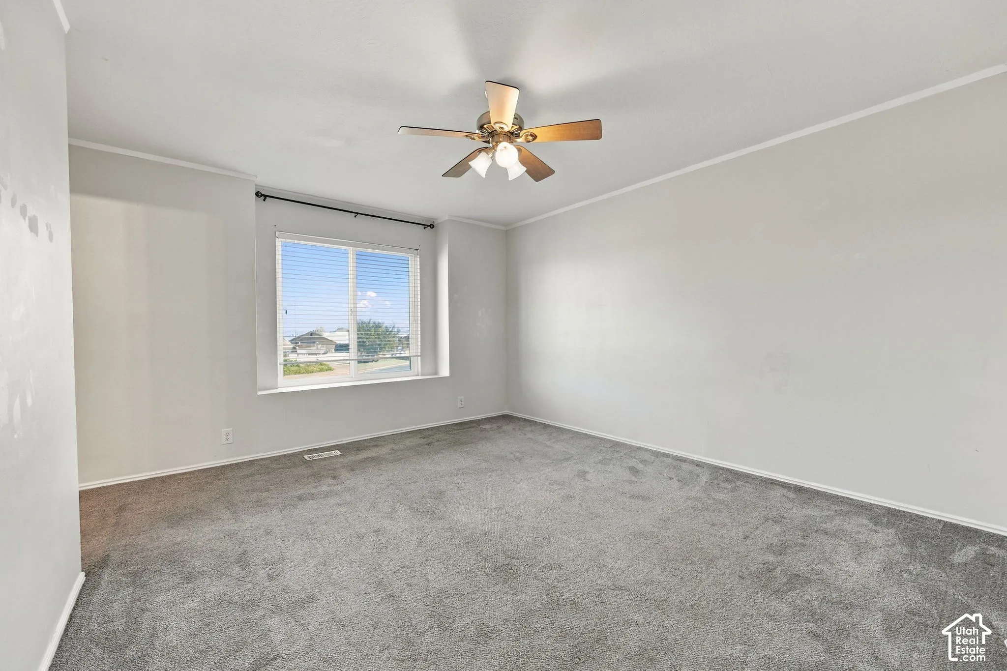 Neutral-toned interior space featuring neutral wall-to-wall carpeting, a large picture window, and a central ceiling fan with integrated lighting