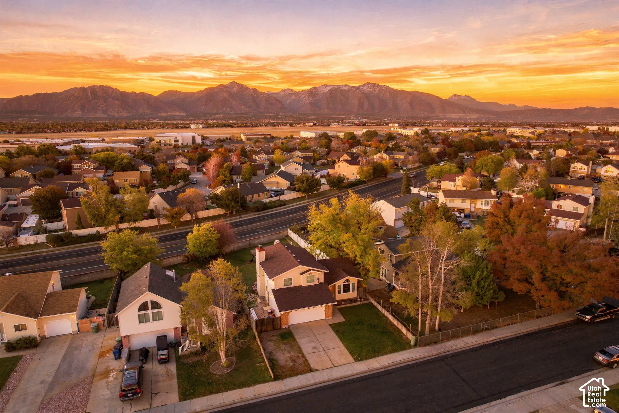Aerial perspective of a multi-story residence featuring a two-car garage, pitched roofline, brick chimney, and prominent mountain backdrop