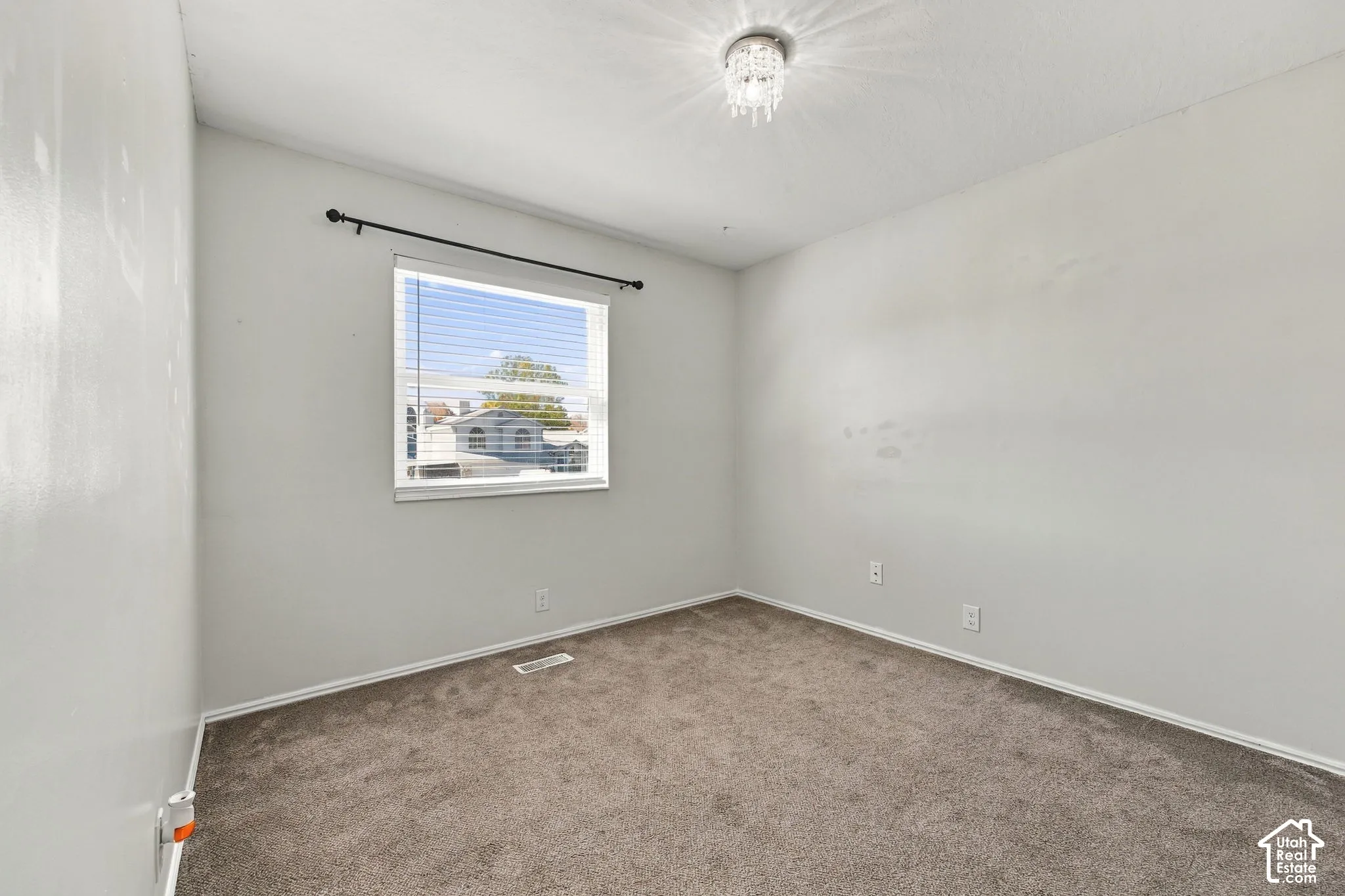 Neutral wall-to-wall carpeting, window with installed horizontal blinds, and a crystal-accented flush-mount ceiling light fixture