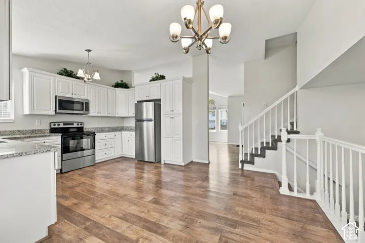 Kitchen featuring white cabinetry, stone-finish countertops, stainless steel appliances, wood-finish flooring, and a multi-arm chandelier