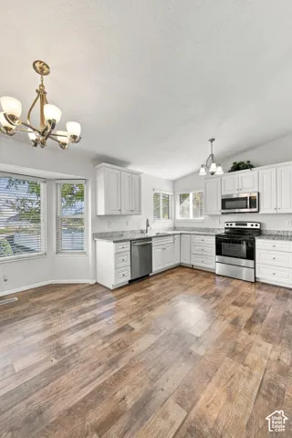 Kitchen featuring white cabinetry, stone-finish countertops, stainless steel appliances, wood-finish flooring, and bay window detailing