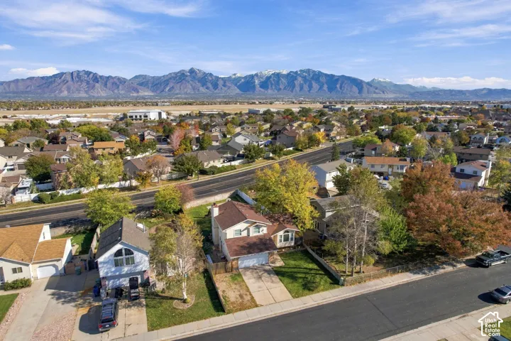 Aerial perspective of residential property featuring a pitched roof, attached garage, concrete driveway, and expansive mountain range backdrop
