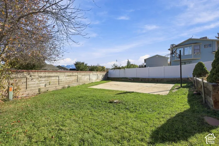 Fenced backyard featuring a concrete sports court, masonry perimeter wall, and vinyl fencing