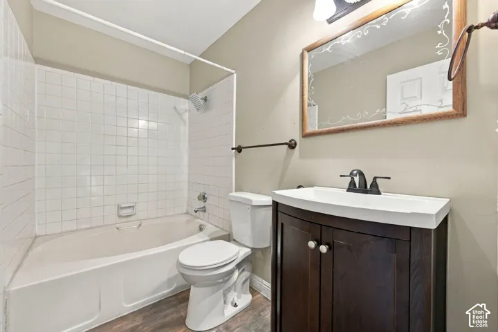 Bathroom featuring a dark wood-finish vanity with a white rectangular sink, a tub-shower combination with white tiled surround, and wood-finish flooring
