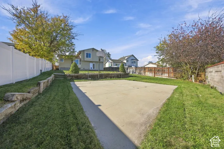 Expansive backyard featuring a concrete sport court, tiered timber retaining walls, mature landscaping, and vinyl perimeter fencing