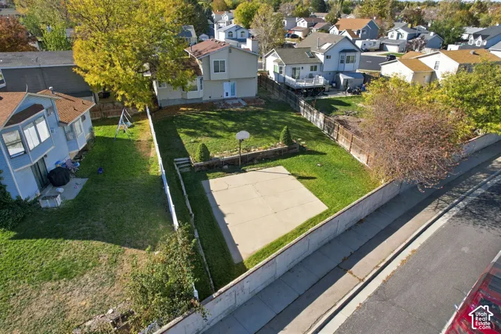 Fenced backyard featuring a concrete sport court, tiered stone retaining wall, mature landscaping, and an expansive lawn