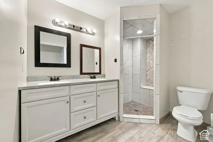 Dual-sink vanity with stone countertop and white cabinetry, accompanied by a walk-in shower featuring herringbone-patterned tile accents and wood-finish flooring