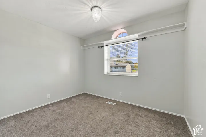 Room featuring neutral carpeting, a crystal-accented flush-mount light fixture, a window with an arched transom, and integrated shelf storage