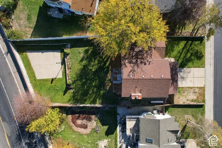 Aerial perspective of property featuring a fenced backyard, concrete parking area, mature trees, and shingle roofing