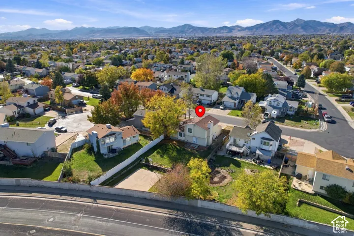 Aerial perspective of suburban property featuring a fenced lot, mature trees, and a mountain range backdrop