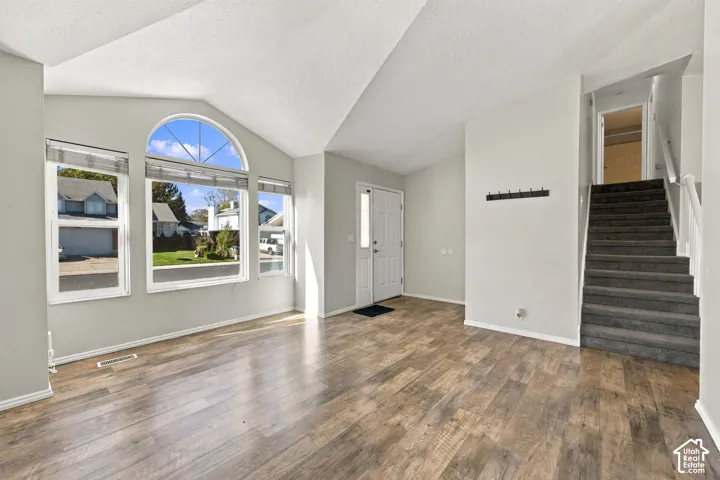 Vaulted ceiling living area featuring wood-finish flooring, an arched window, and a staircase with carpeted treads
