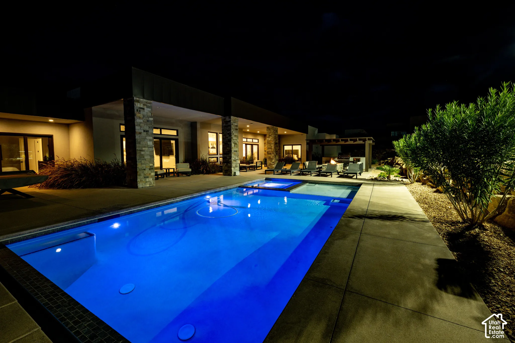 Pool and spa at night, with the covered patio, fire pit and outdoor kitchen beyond
