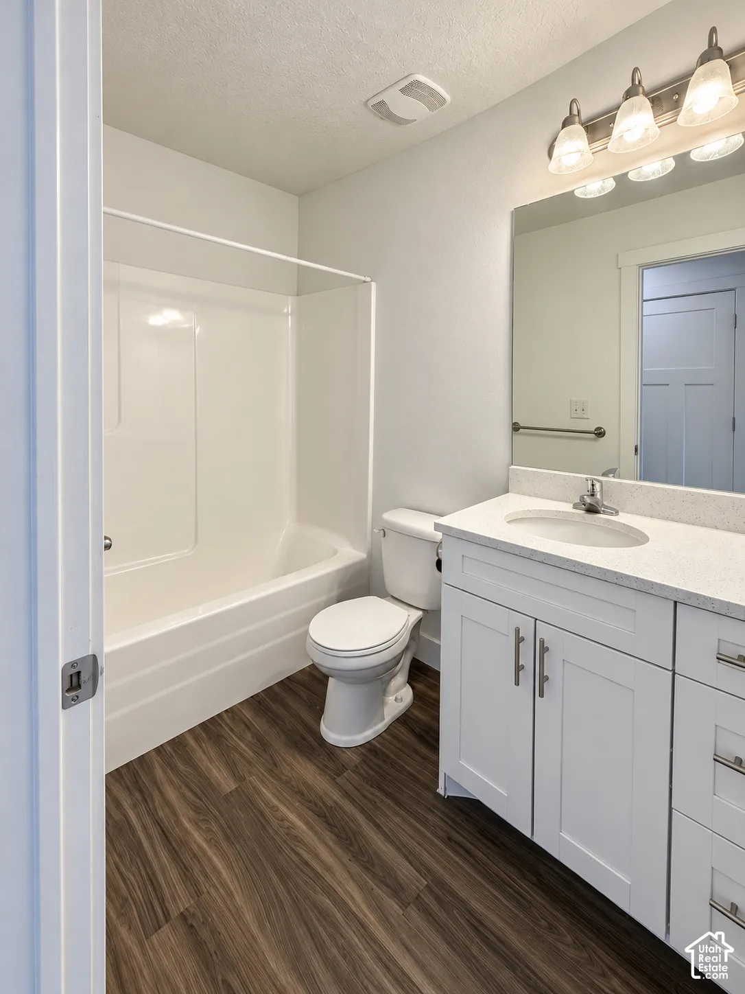 Bathroom featuring wood-finish flooring, white cabinetry with metallic hardware, stone-composite countertop, integrated porcelain sink, and a combination tub and shower surround