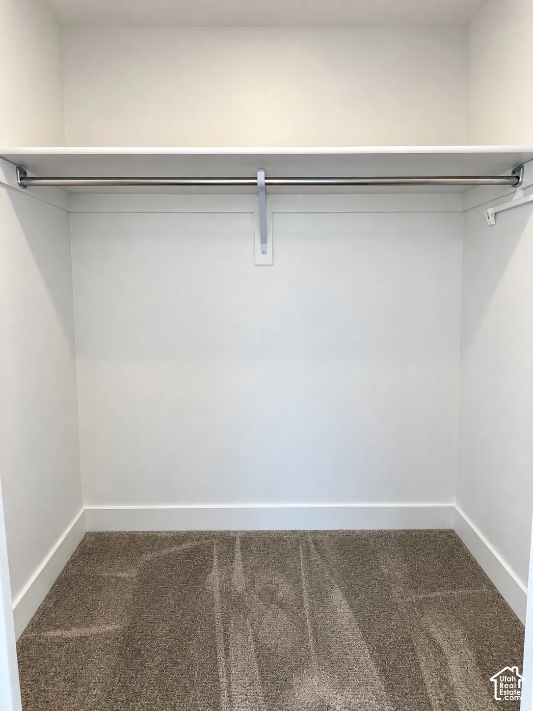 Closet interior featuring neutral-toned carpeting, white walls, and a built-in shelf with a metal rod