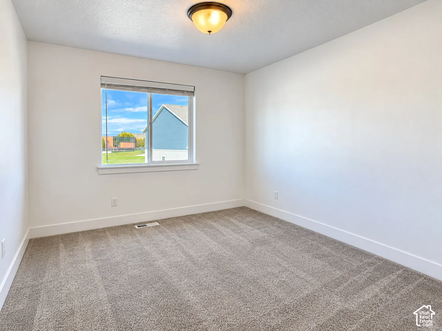 Neutral interior featuring neutral carpeting, a single window with a roller shade, and a flush-mount ceiling light fixture