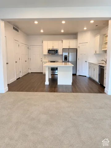 Kitchen featuring white shaker-style cabinetry, central island with quartz countertop, stainless steel appliances, and wood-finish flooring