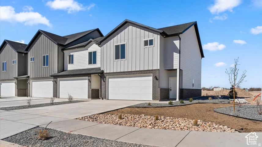Modern multi-family exterior featuring vertical and horizontal siding, dark brick masonry base, composite shingle roof, and attached multi-car garages