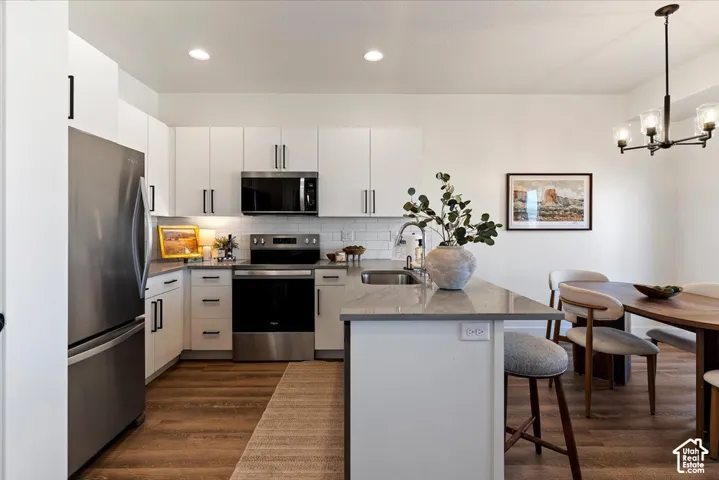 Kitchen featuring white cabinetry with matte black hardware, stone-finish countertops, stainless steel appliances, subway tile backsplash, and wood-finish flooring