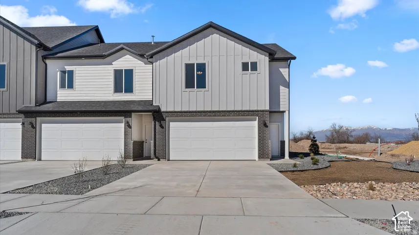 Two-story exterior featuring a mix of vertical board-and-batten siding and dark brick masonry, complemented by a concrete driveway and an attached two-car garage