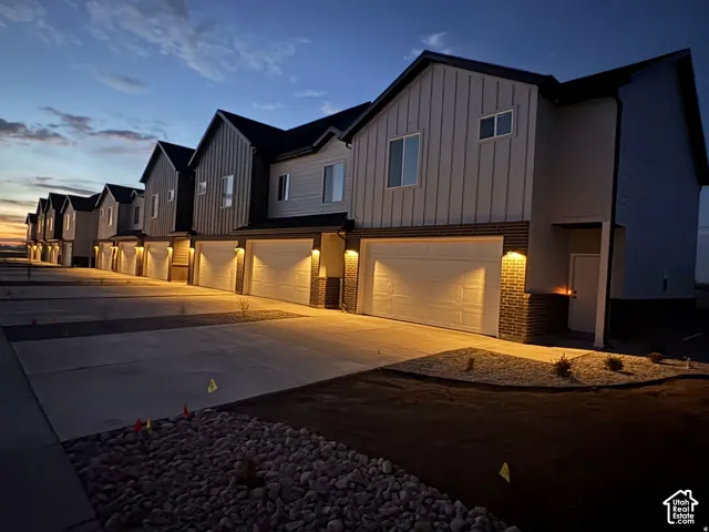 Multi-unit exterior featuring vertical siding, brick accents, attached multi-car garages, and concrete driveway paving